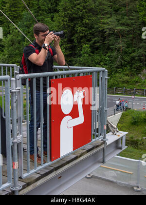 Young caucasian male taking a picture with his camera from a viewpoint designated with a large viewpoint sign. Canton of Uri, Switzerland. Stock Photo