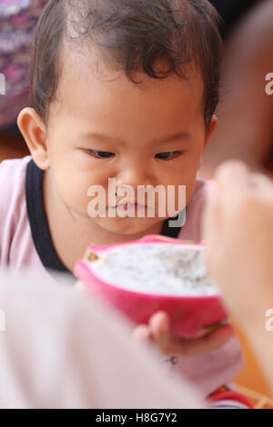 Asian baby eating a dragon fruit with happily,concept of health and foods of the children. Stock Photo