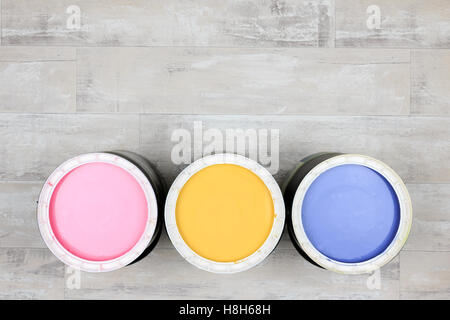 Looking down on three open paint cans of coloured paint stood on a shabby style wood floor Stock Photo