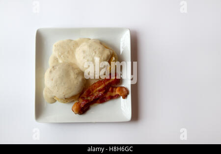 Biscuits and Gravy with two slices of Bacon on a white plate isolated on a white background Stock Photo