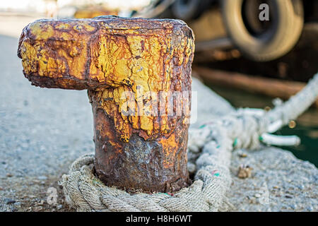 Old Rusty Bollard with Frayed Ship Rope at the Harbor. Nautical Background. Stock Photo