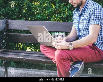Young Man working on his laptop sitting on the bench in park Stock Photo