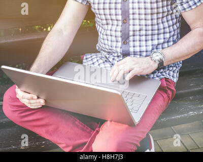 Young Man Sitting On a Bench and Working On His Laptop Stock Photo