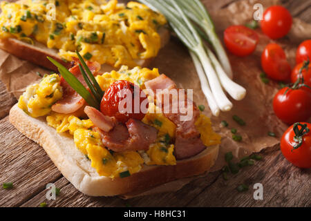 Homemade sandwich with scrambled eggs, bacon and tomatoes close-up on the table. horizontal Stock Photo