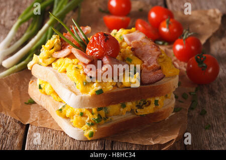 double sandwich with scrambled eggs, bacon and tomatoes close-up on the table. Horizontal Stock Photo