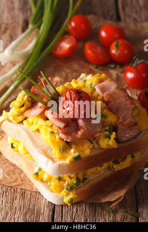 double sandwich with scrambled eggs, bacon and tomatoes close-up on the table. vertical Stock Photo