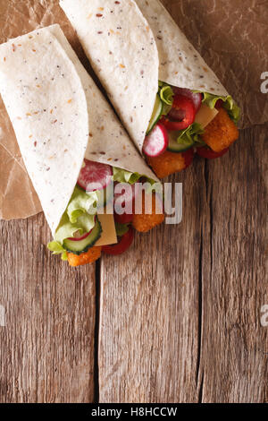 Sandwich roll with fish fingers, cheese and vegetables close-up on the table. vertical view from above Stock Photo