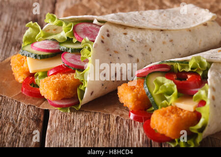 Tortilla roll with fish fingers, cheese and vegetables close-up on the table. Horizontal Stock Photo
