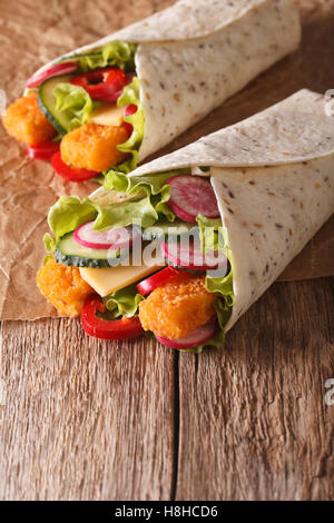 Tortilla roll with fish fingers, cheese and vegetables close-up on the table. vertical Stock Photo