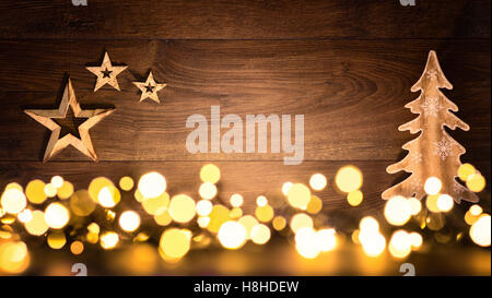 Christmas background with wooden ornaments arranged on a dark wood board and bokeh lights shining in the foreground Stock Photo