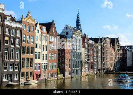 A sightseeing boat motors along in front of the famous houses lining the edge of the Damrak canal basin, Amsterdam, Netherlands Stock Photo