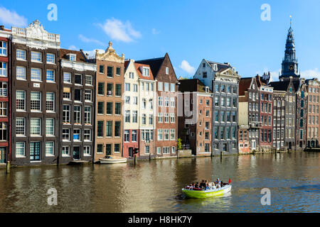 A sightseeing boat motors along in front of the famous houses lining the edge of the Damrak canal basin, Amsterdam, Netherlands Stock Photo