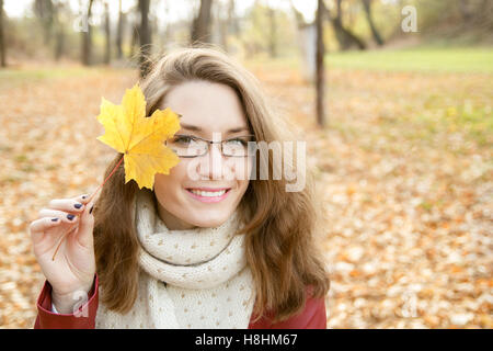 Beautiful young woman in autumn park portrait holding autumn leaf Stock Photo