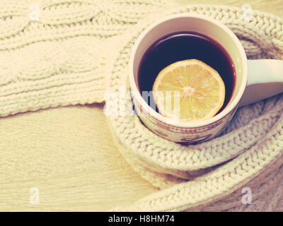 Cup of hot tea with lemon dressed in warm winter scarf Stock Photo