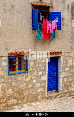 Laundry driying in sun, washing line hanging from blue windows and blinds. Stock Photo