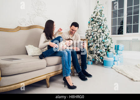 Cheerful family sitting in the living room having fun with the digital tablet that Santa Claus brought her, behind the decorated christmas tree Stock Photo