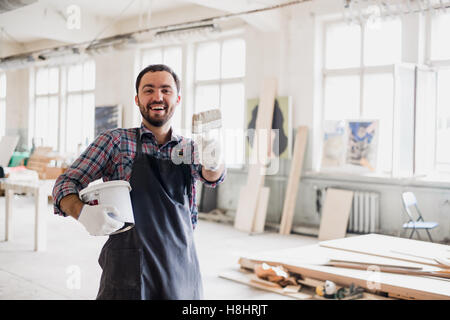 Happy young painter holding paint brush and showing it to camera Stock Photo