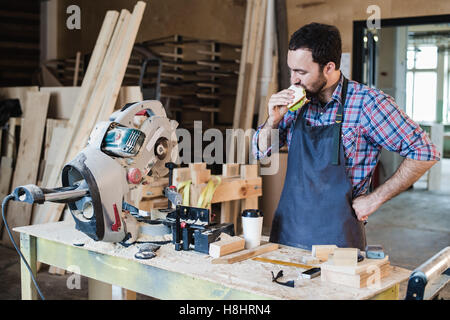 Cheerful carpentry worker having lunch eating sandwich in a workshop Stock Photo