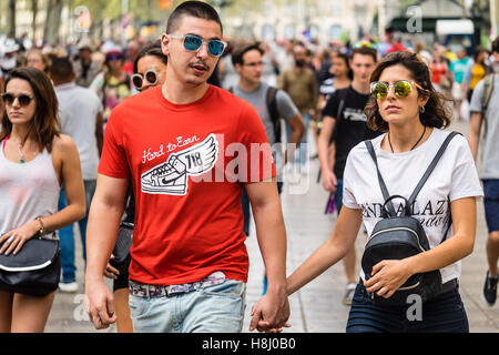 Two tourists, a man and a woman, wearing sunglasses, walk with the crowd of people along the La Rambla walking street. Stock Photo