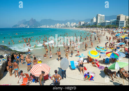 RIO DE JANEIRO - MARCH 01, 2015: Beachgoers relax on the Arpoador end of Ipanema Beach with colorful umbrellas along the skyline Stock Photo