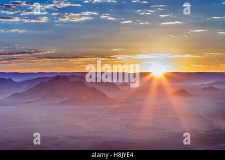 Sunrise with the suns rays peeping over the horizon  in Sossusvlei Namibia giving a lunar appearance to the landscape Stock Photo