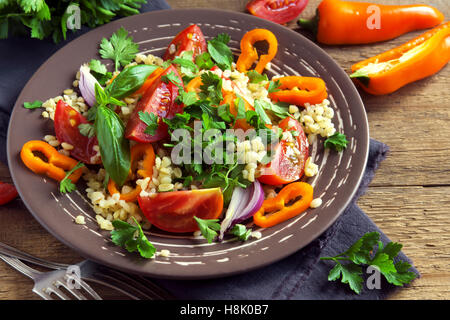 Fresh organic tomato and couscous salad with vegetables and greens - healthy vegetarian salad on rustic plate close up Stock Photo