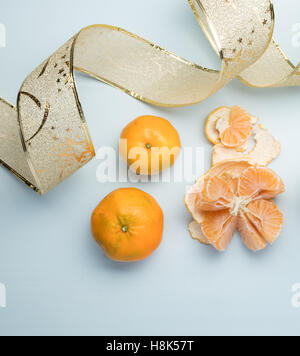 mandarins on a blue table, one of them open showing its freshness, on the left side a Christmas ribbon Stock Photo