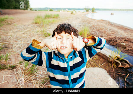 little cute boy smiling thumbs up on lake shore at summer vacati Stock Photo