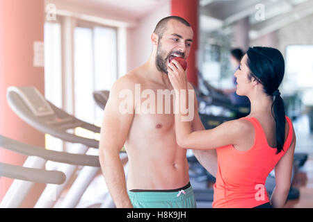 Happy couple in gym feeding each other with apple Stock Photo