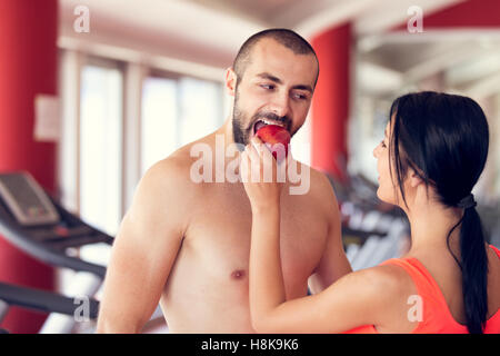 Happy couple in gym feeding each other with apple Stock Photo