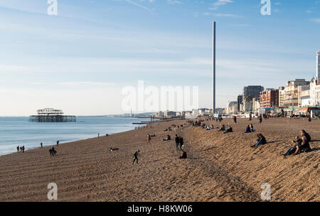View of Brighton Beach, looking towards the West Pier and i360 with people enjoying sunshine sitting on the pebbles and shingle Stock Photo