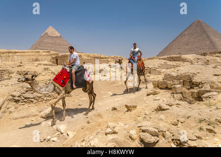 Cairo, Egypt Tourists riding camels walking through the desert with the Great Pyramids of Giza in the background. These particul Stock Photo