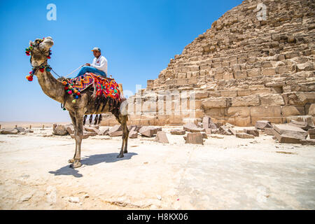 Cairo, Egypt Camel and its rider resting in the desert beside ruble at the base of one of the Great Pyramids of Giza. Stock Photo