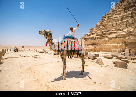 Cairo, Egypt Camel and its rider resting in the desert beside ruble at the base of one of the Great Pyramids of Giza. Stock Photo