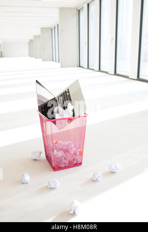 Laptop and crumpled papers in garbage can at office Stock Photo
