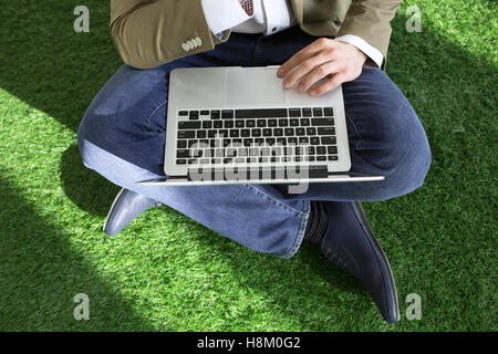 High angle low section of businessman using laptop while sitting on turf Stock Photo