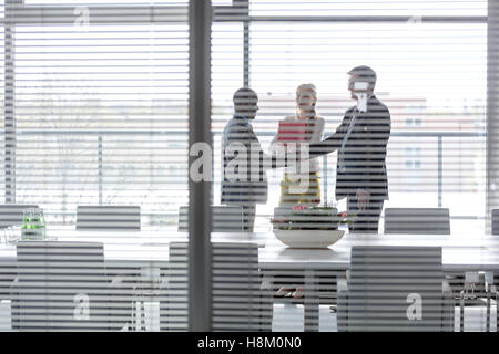 Businessmen shaking hands by female colleagues in board room seen through jalousie window Stock Photo