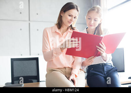 Young businesswomen reading file while sitting on desk in office Stock Photo
