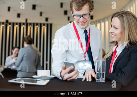 Businesswoman looking at colleague using smart phone during coffee break at convention center Stock Photo
