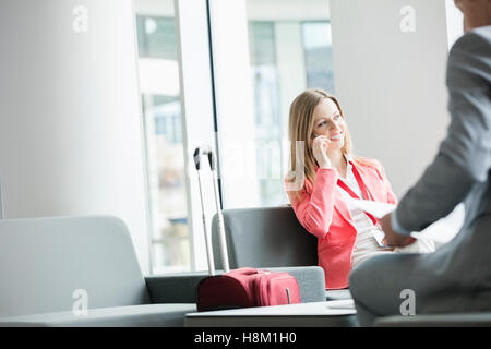 Smiling businesswoman using smart phone while sitting at lobby in convention center Stock Photo