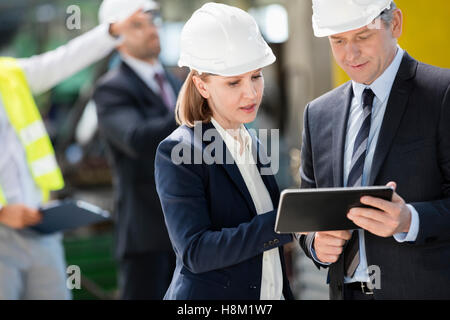 Businessman and businesswoman using digital tablet with colleagues in background at industry Stock Photo