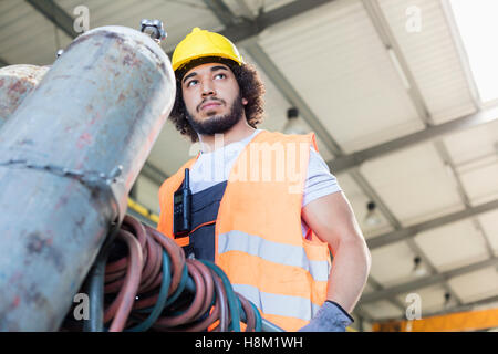 Low angle view of young manual worker moving gas cylinder in metal industry Stock Photo