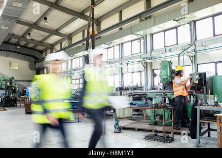 Blurred motion of business people walking with manual worker in background at industry Stock Photo