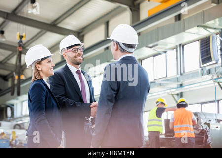 Businessmen shaking hands with workers working in background at metal industry Stock Photo