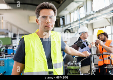 Portrait of mid adult worker wearing protective eyewear with colleagues in background at industry Stock Photo