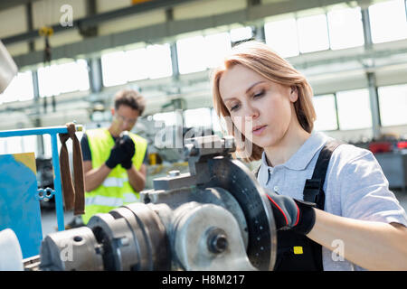 Mature female worker working on machinery with colleague in background at industry Stock Photo