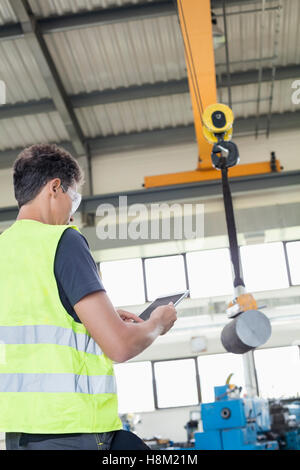 Mature manual worker with digital tablet operating crane to lift steel in industry Stock Photo