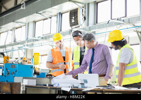 Supervisor with workers examining blueprints at table in industry Stock Photo