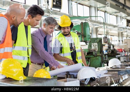 Male supervisor with workers discussing over blueprints in industry Stock Photo