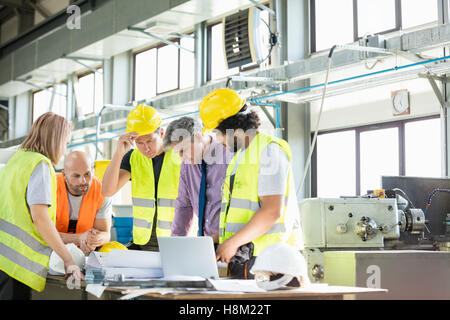 Male architect and manual workers discussing over blueprints in industry Stock Photo